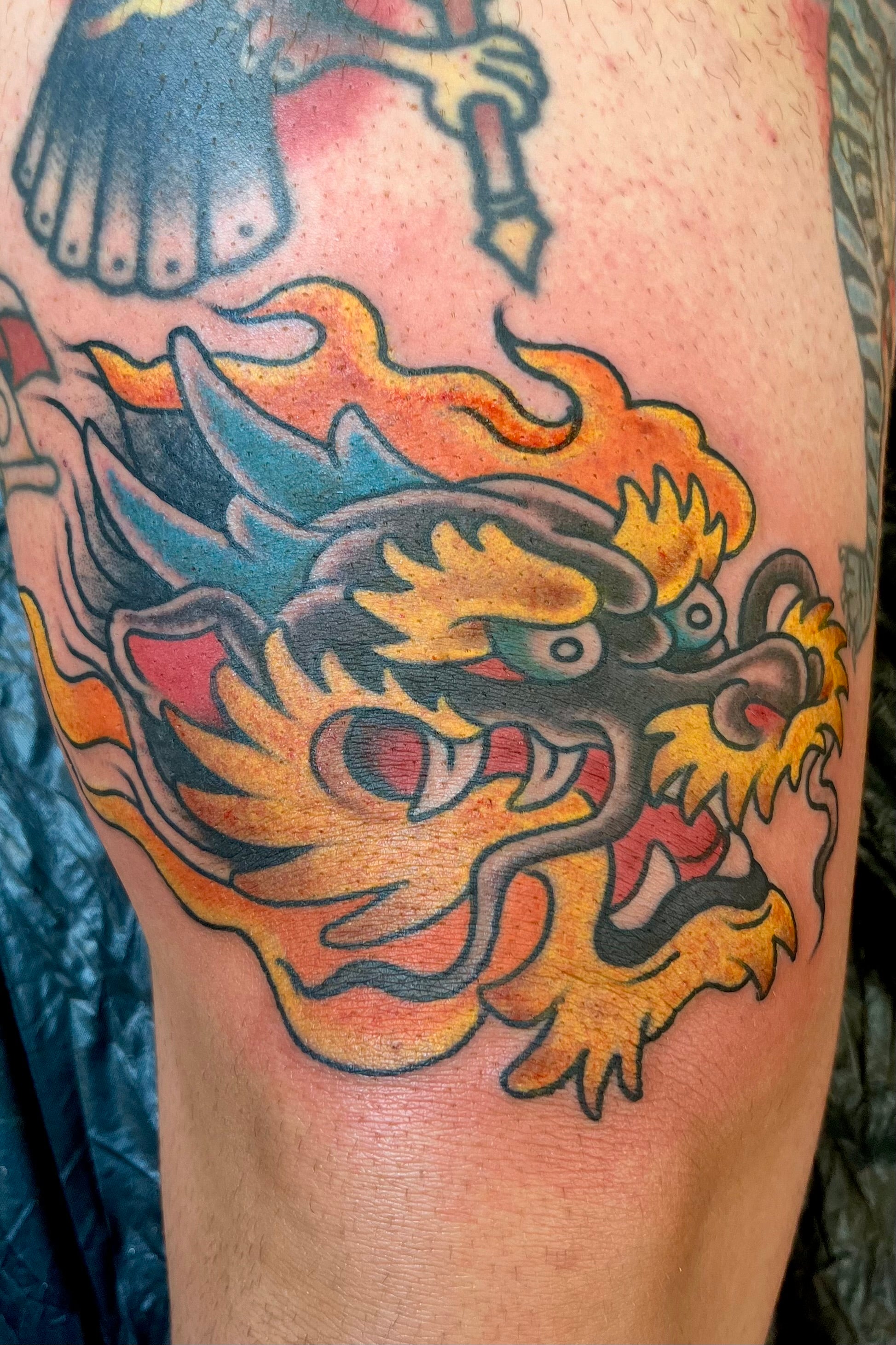 Bold American traditional and Japanese classic tattoo of a dragon head surrounded by flames in colour. Tattooed in London 