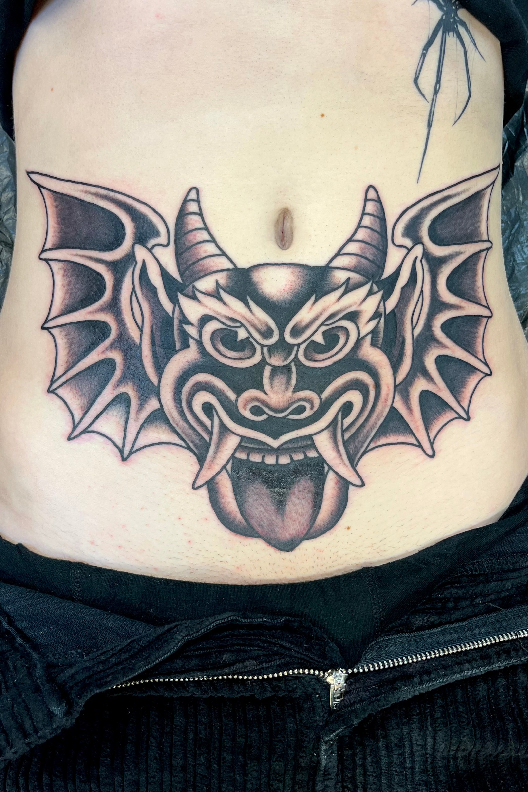 Bold American traditional classic Black and grey stomach tattoo of a Ben Corday demon head with wings. Tattooed in London at frith street tattoo