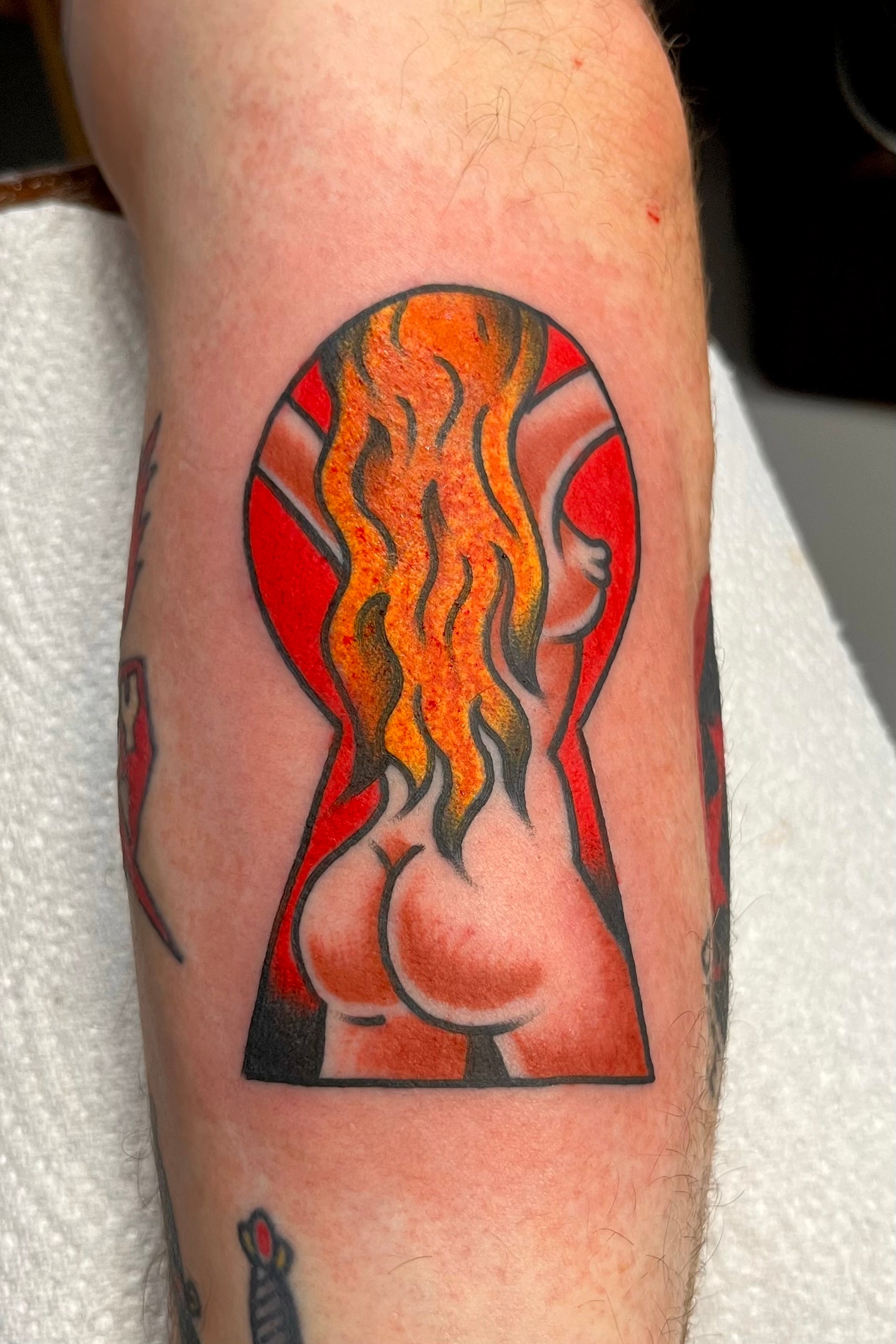 a bold american traditional nude pin up girl viewed through a keyhole in full colour. tattooed in london at frith street tattoo