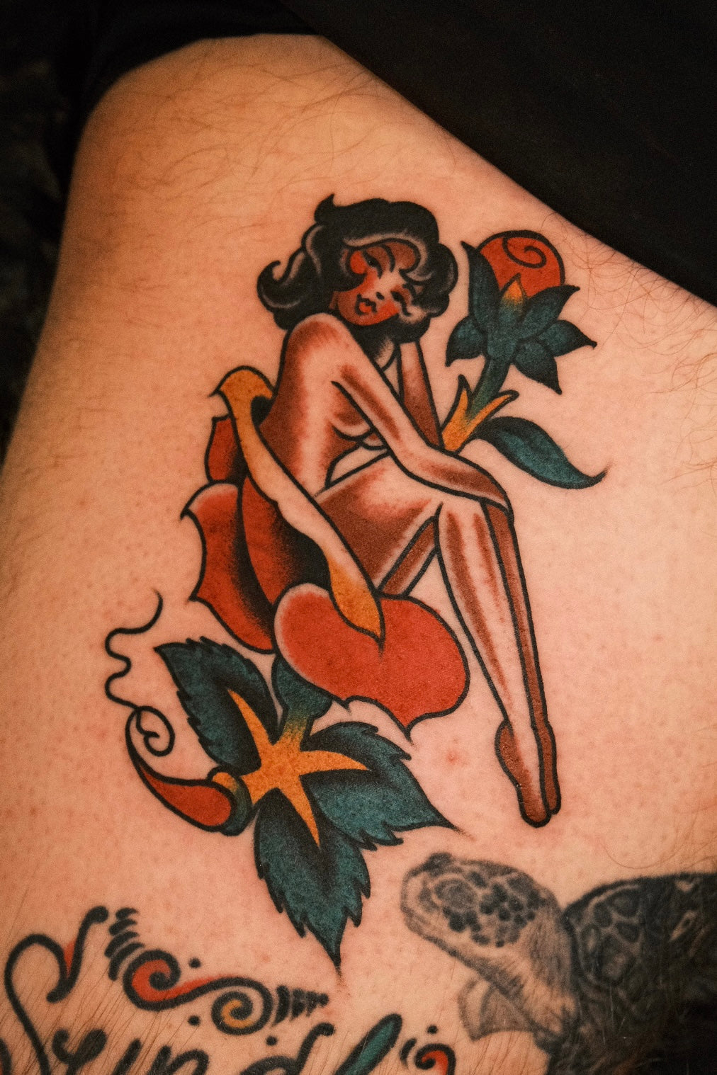 Bold American traditional classic pin up girl in a rose tattoo in colour. Done in London by jake cordal at frith street tattoo