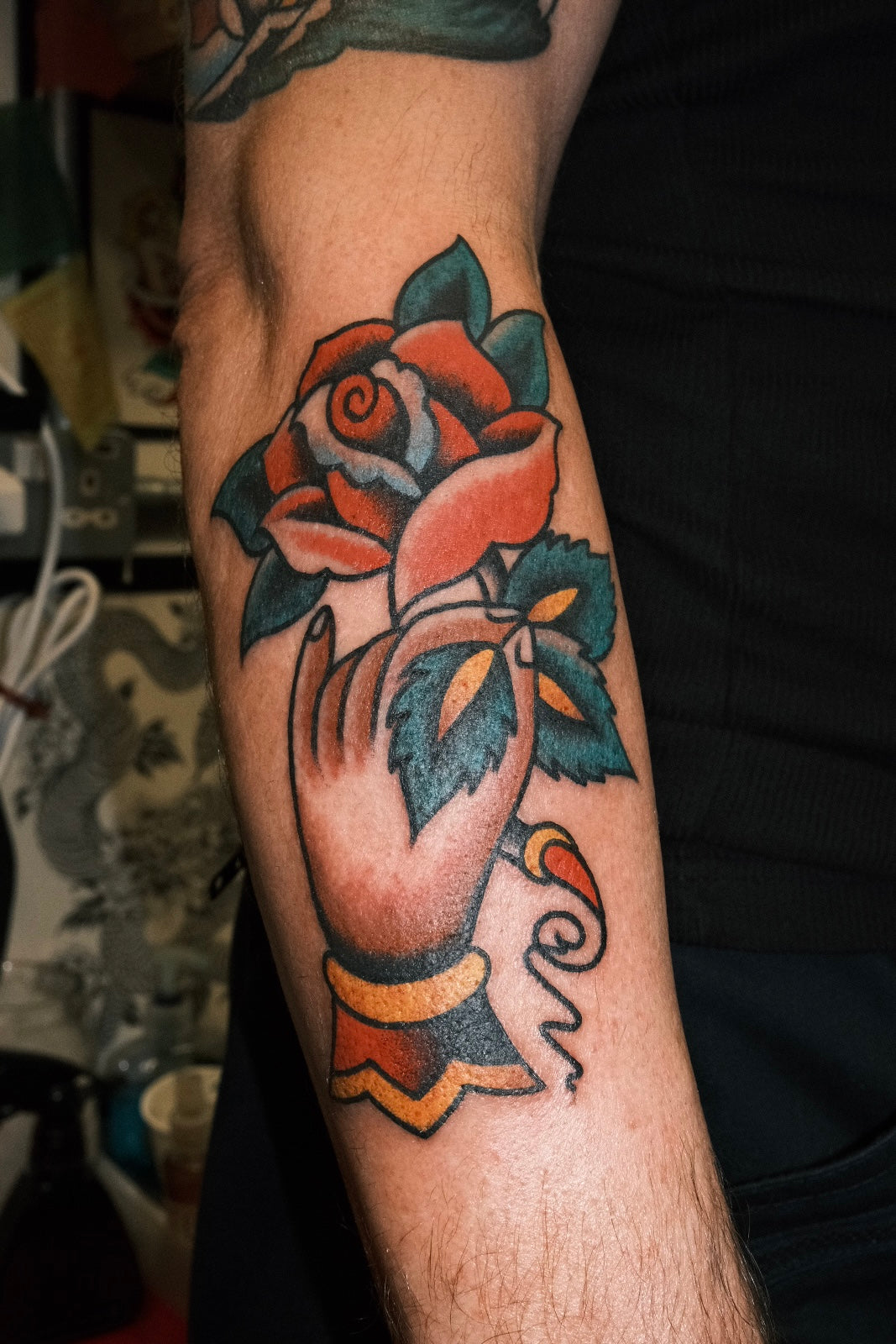 a full colour bold american traditional hand holding a rose tattoo as part of a traditional patchwork sleeve. by jake cordal in frith street tattoo